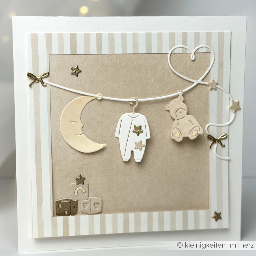 Handgefertigte Babykarte von Alexandra Renke mit Mond, Onesie, Teddybär und Sternen an einer Schnur in neutralem Beige und Weiß, akzentuiert mit Designpapier Streifen warmgrau für einen charmanten Touch.