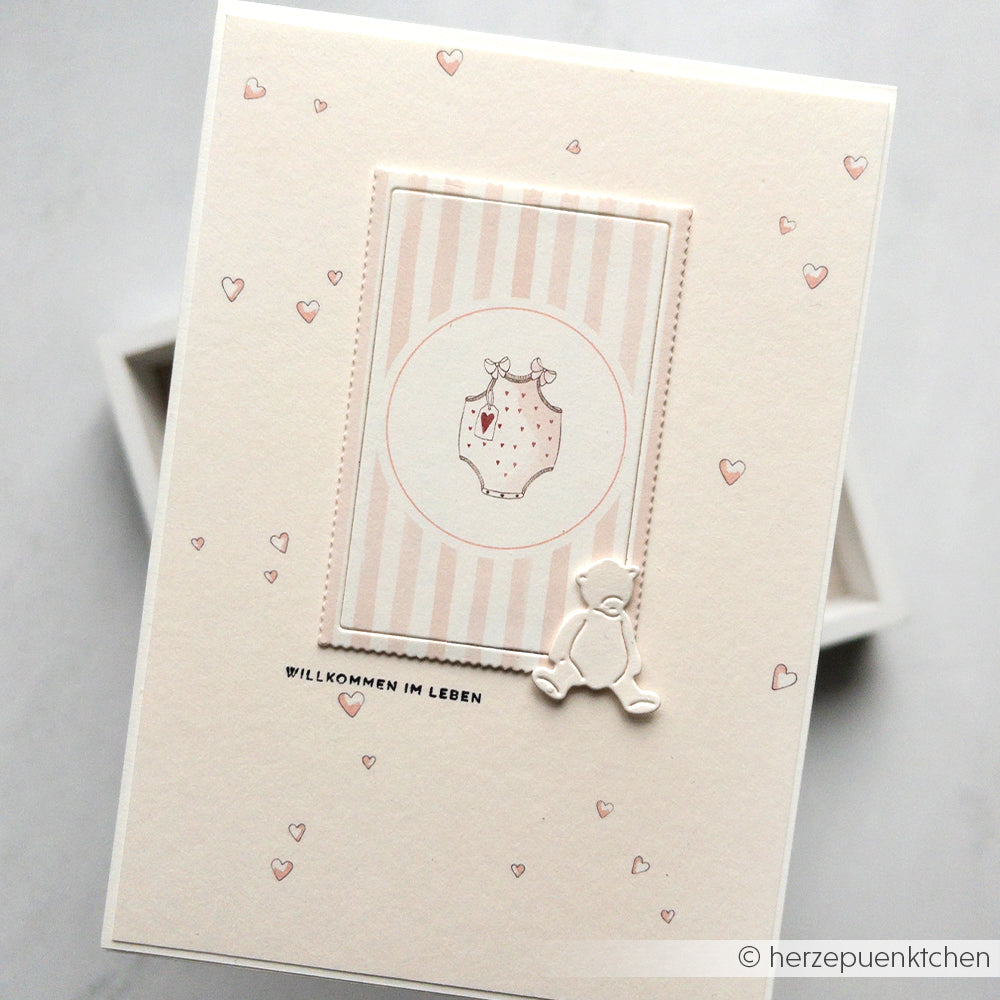 Cremefarbene Babykarte von Alexandra Renke mit Herzen, Onesie und Teddybär aus Designpapier Herzchen rosa. Mit dem Text "Willkommen im Leben". Ideal für Papierprojekte zur Begrüßung eines Neuankömmlings.
