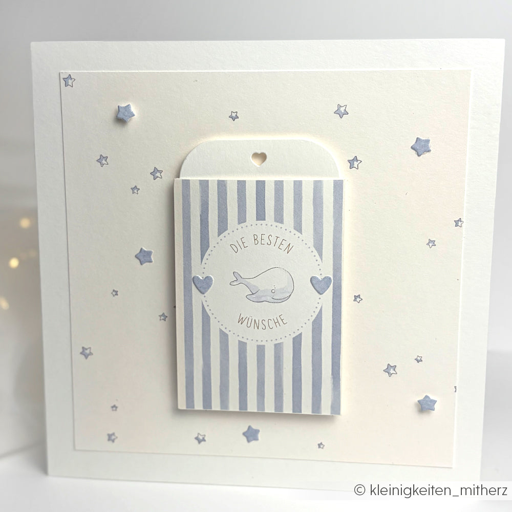 Quadratische Karte von Alexandra Renke aus hellblauem Sternenhimmel-Designpapier mit blauen Sternen, Streifen, einer Wal-Illustration und "Die besten Wünsche" - ideal zum Papierbasteln oder Buchbinden.
