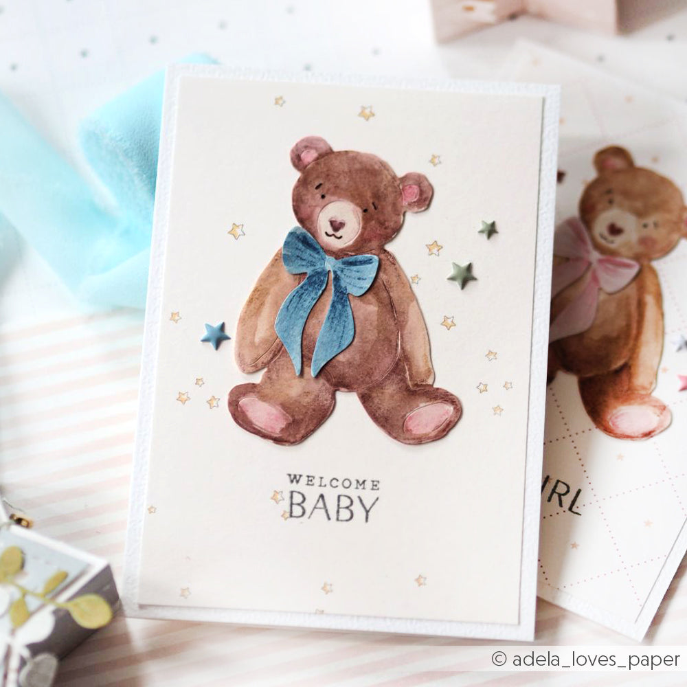 Grußkarte von Alexandra Renke mit einem Teddybär mit blauer Schleife und dem Text "Welcome Baby", umgeben von Sternen - ideal für Papierprojekte oder den Druck auf charmantem Sternenhimmel-Designpapier.