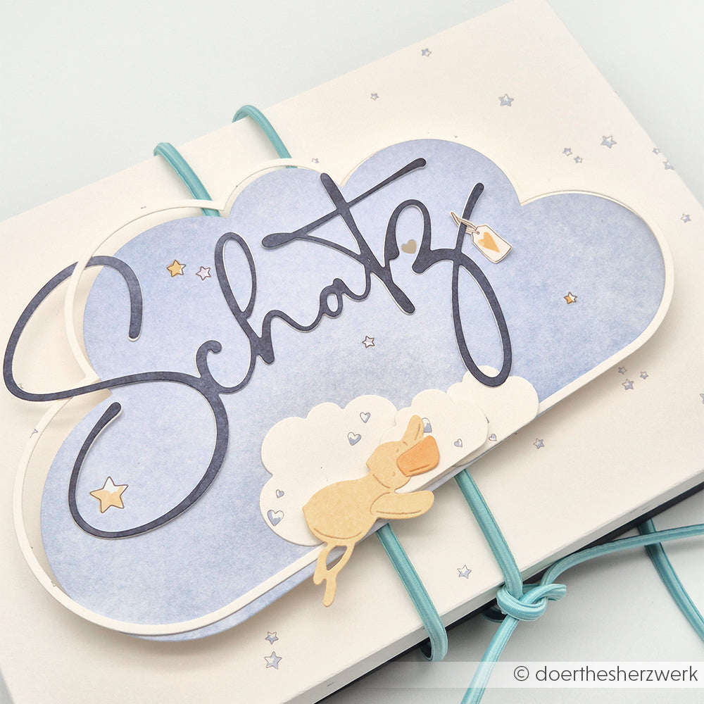 Eine wolkenförmige Karte von Alexandra Renke mit Schatz und einem kleinen Bären, der auf Wolken mit Sternen schläft - ideal für Papierprojekte oder in Kombination mit Mimi Blauer Himmel Designpapier.