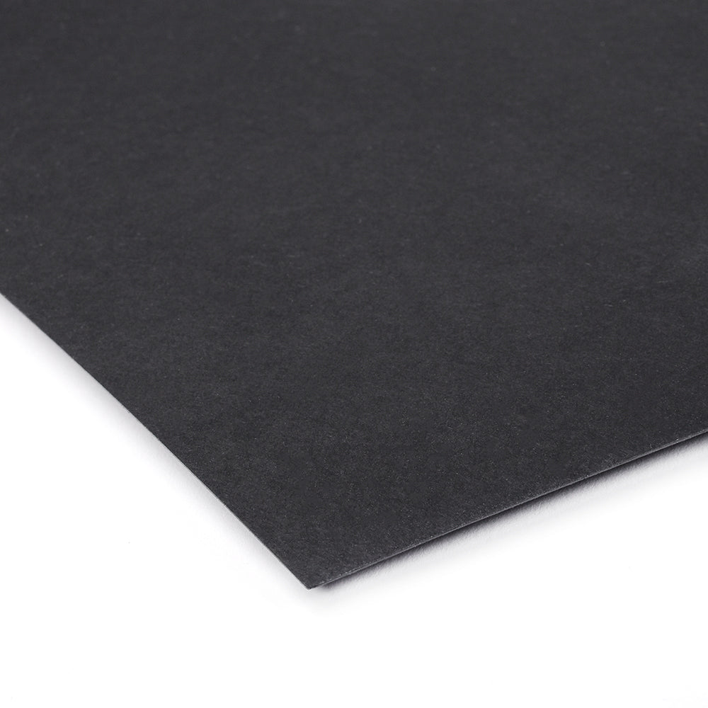 Ein Bogen schwarzer Alexandra-Renke-Karton auf weißer Oberfläche, aus einem Winkel fotografiert - perfekt für Buchbinden oder Schachtelbau-Projekte.