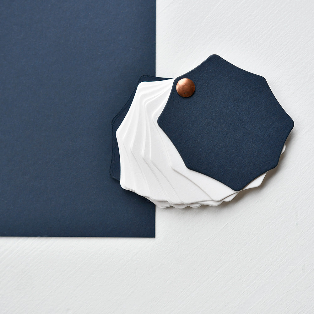 Sechseckige marineblaue und weiße Muster sind auf einer weißen Fläche neben einem 700 g/m² starken marineblauen Karton von Alexandra Renke angeordnet, ideal für Schachtelbau- oder Buchbinden-Projekte.