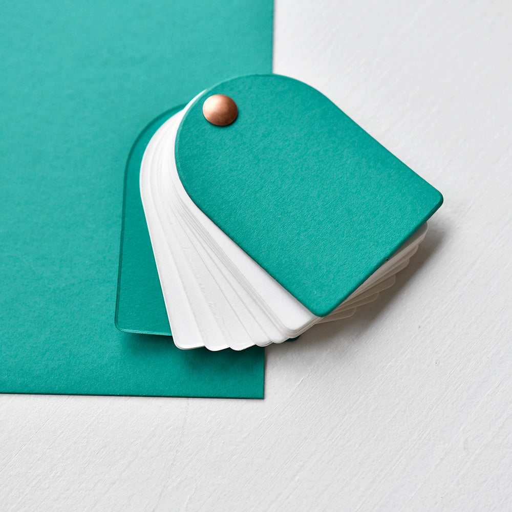 Das Papiermusterbuch Alexandra Renke teal ist mit 700g/m² Karton und weißen Musterbögen ausgestattet, ideal für Buchbinden, und wird auf weißem und tealem Hintergrund gezeigt.