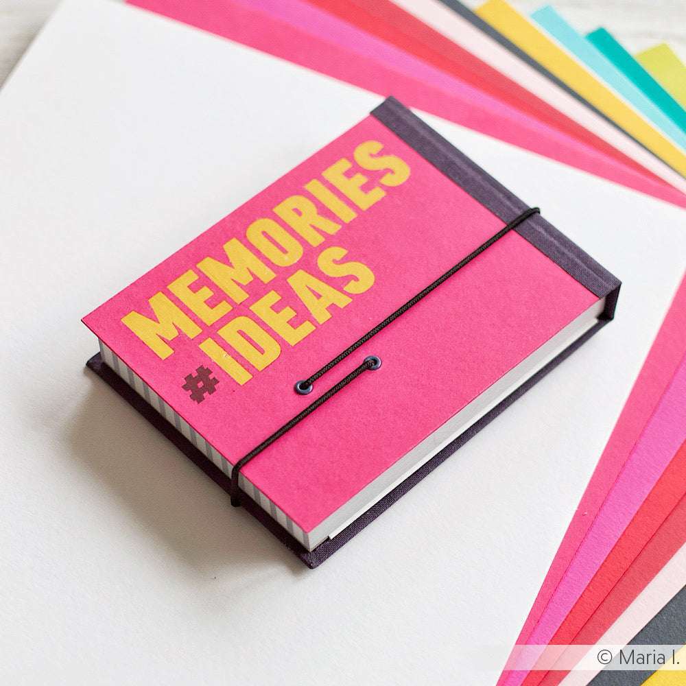 Ein pinkfarbenes Notizbuch von Alexandra Renke mit der Aufschrift MEMORIES #IDEAS liegt auf bunten Spezialpapierblättern und verleiht jeder Seite eine einzigartige Note.