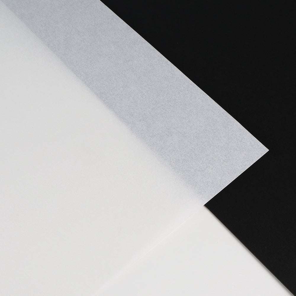 Ein transluzentes Blatt Alexandra Renke Pergamentpapier, das über schwarze und weiße Oberflächen gelegt wird, bietet einen starken Kontrast - perfekt für luxuriöse Verpackungen oder hochwertige Drucke.