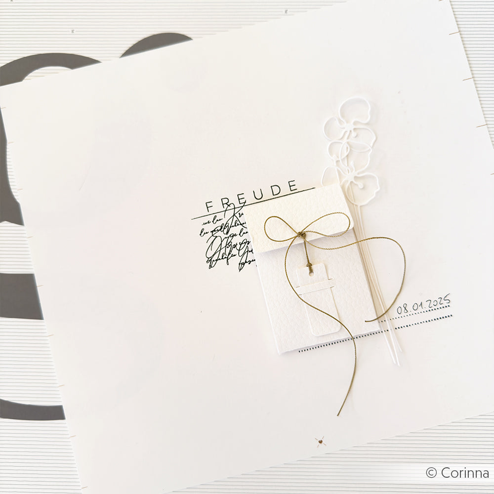 Minimalistische weiße Karte aus strukturiertem Karton mit goldener Schnur, klaren Luftballons und "FREUDE" mit dem Datum 08.04.2025.