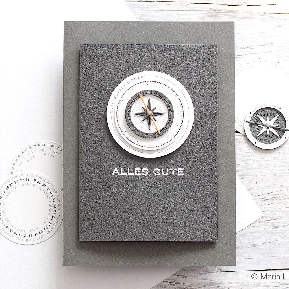 Eine graue Grußkarte von ☆ aus strukturiertem Cardstock mit einem Kompassmotiv und dem Text "ALLES GUTE" auf der Vorderseite.