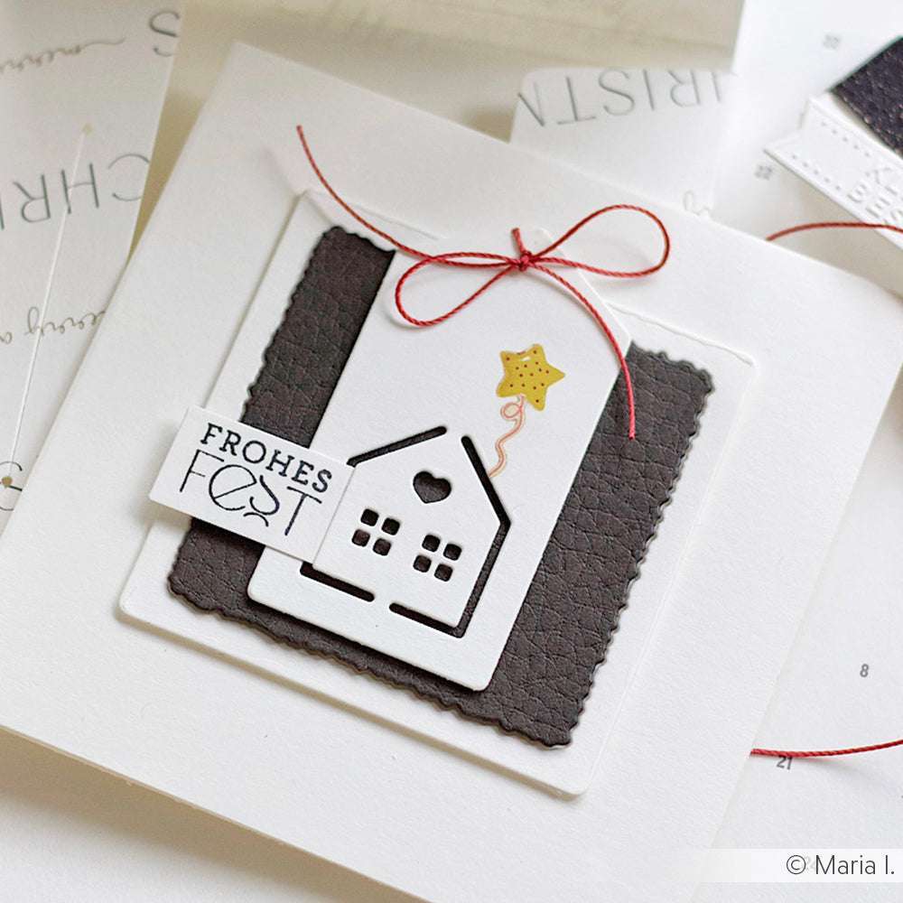 Eine handgefertigte ☆ Karte aus 3D-geprägtem Papier mit einem Hausausschnitt, einem Sternenballon, dem Anhänger "Frohes Fest" und einer roten Schleife.