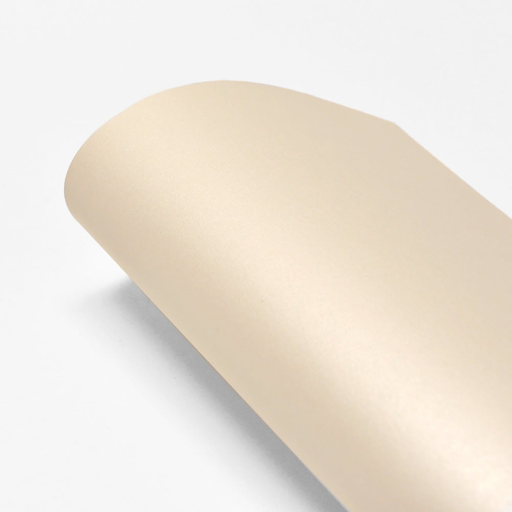 Ein gerolltes Blatt glattes, beiges ☆ Schimmerpapier (310g/m²) für Karten liegt auf einem weißen Hintergrund.