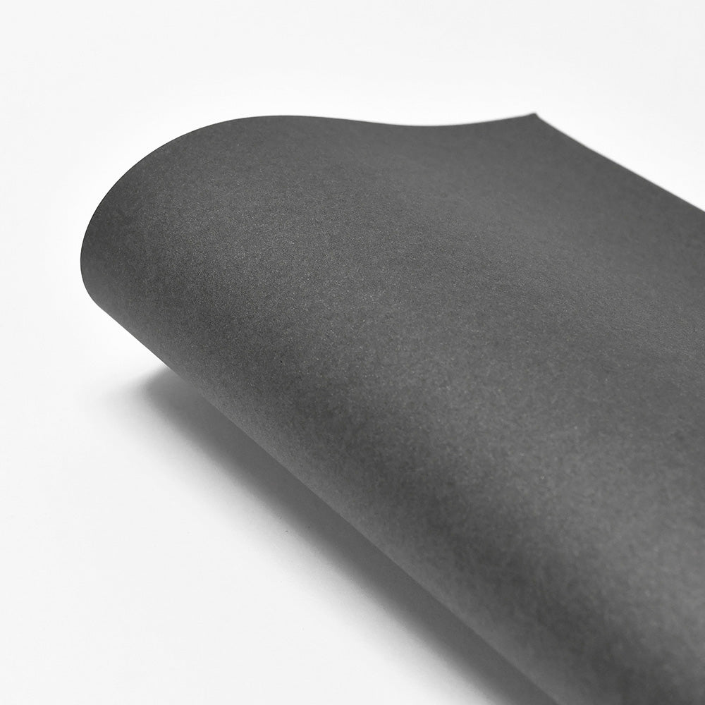 Ein Blatt ☆ FSC-zertifiziertes 310g/m² Papier, schwarz mit einer gewellten Ecke, liegt auf einem weißen Hintergrund.