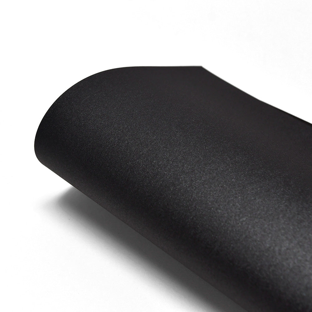 Ein Blatt ☆ mattschwarzes 310g-Papier mit einer gewellten Ecke vor einem weißen Hintergrund.