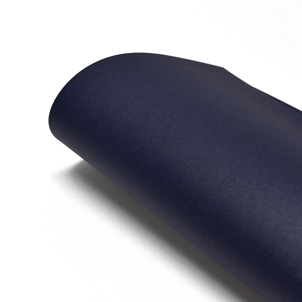 Ein gerollter Bogen ☆ dunkelblaues Schimmer-Effekt Papier, 310g/m², liegt elegant auf einer weißen Fläche.