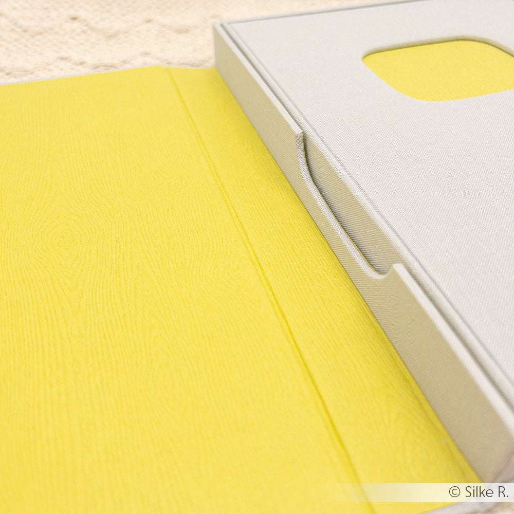 Nahaufnahme einer ☆ gelben strukturierten Mappe aus 300g-Papier, mit einer teilweise geöffneten grauen Schachtel obenauf.