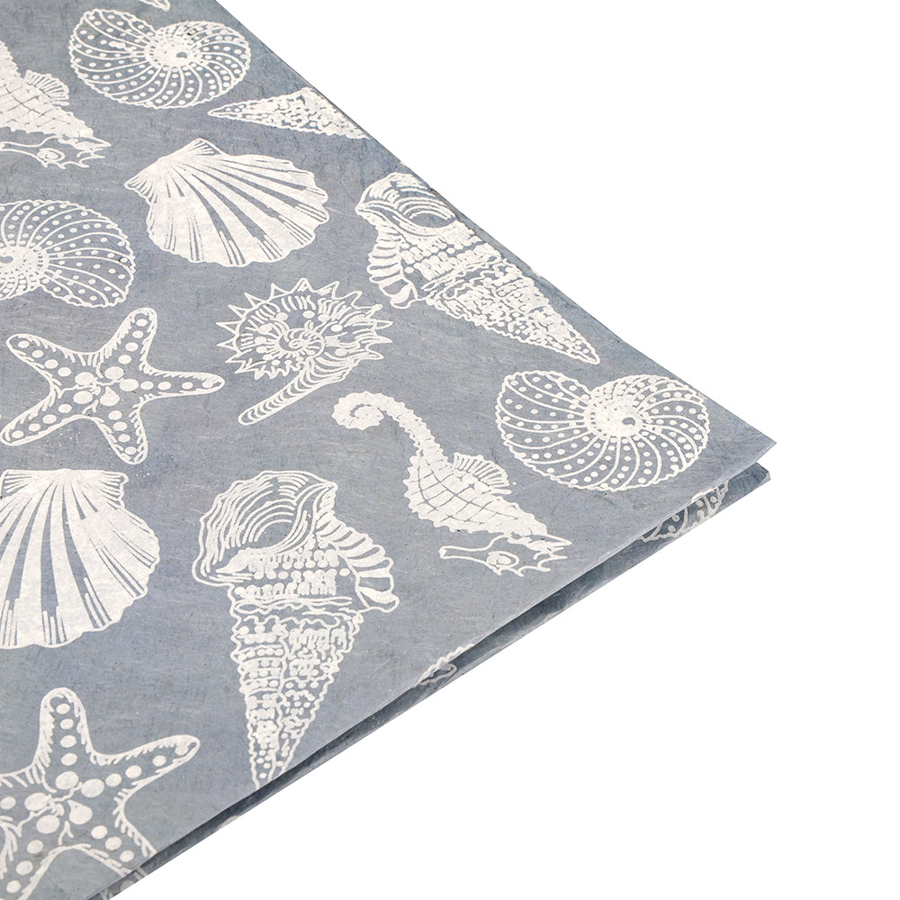 Blauer Stoff, verziert mit weiß aufgedruckten Muscheln, Seesternen und Meereslebewesen, am Rand sorgfältig gefaltet – ein Entwurf von ☆, der den Charme von handgefertigtem Papier oder nachhaltigem Geschenkpapier in künstlerischen Kreationen widerspiegelt.