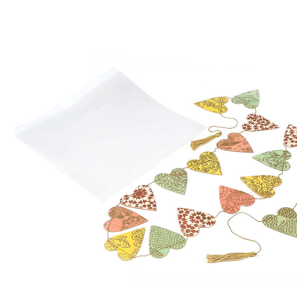Verschönern Sie jeden Raum mit der bunten, gemusterten Herzgirlande aus Nepalpapier mit Quasten. Dieses nachhaltige Produkt wird neben einem transparenten Beutel auf weißem Hintergrund geliefert.