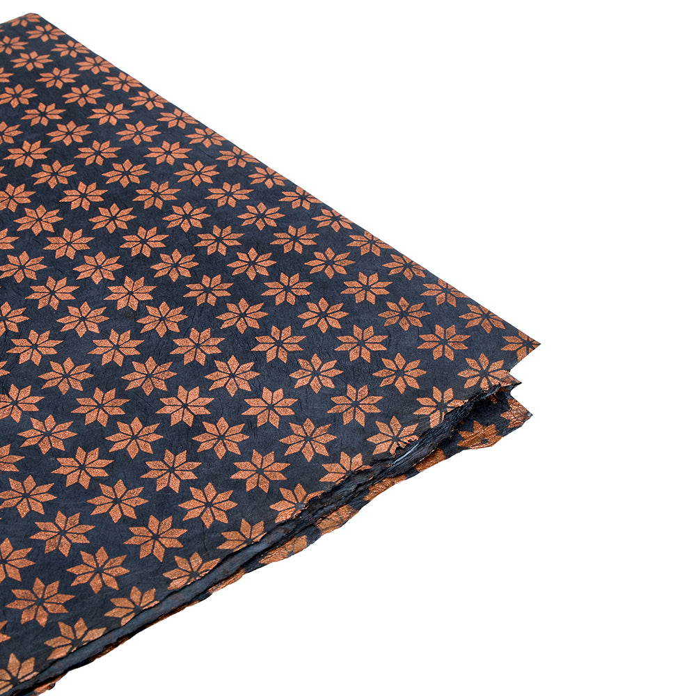 Ein gefaltetes Stück dunkles Nepalpapier von ☆ mit einem orangefarbenen geometrischen Blumenmuster auf Weiß - ideal zum Verschenken mit nachhaltigem Papier.
