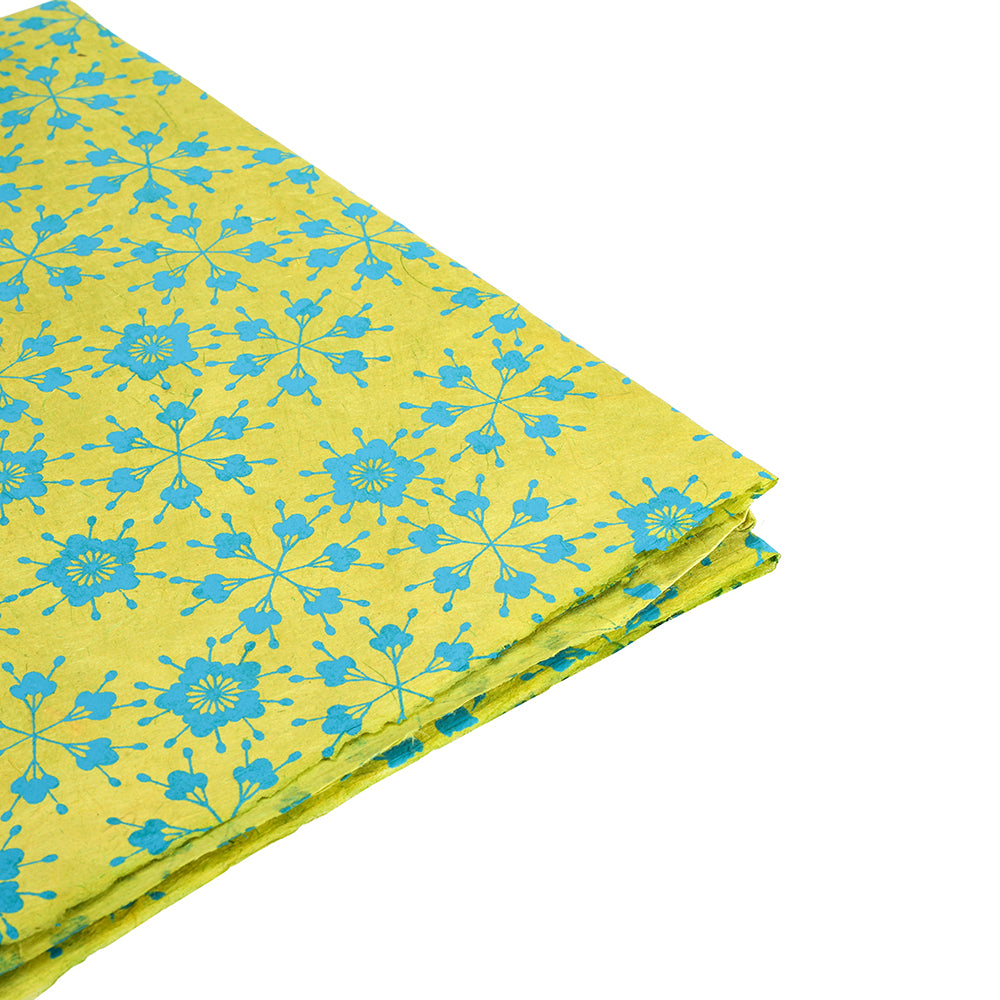 Gefalteter gelber Stoff mit blauen Blumenmustern von ☆, abgebildet auf weißem Hintergrund - ideal für Geschenke Verpacken oder in Kombination mit nachhaltigem Papier.