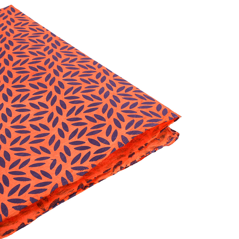 Ein gefaltetes Stück orangefarbenes Nepalpapier von ☆ mit einem sich wiederholenden dunkelblauen Blattmuster auf weißem Grund - perfekt für Geschenkverpackungen.