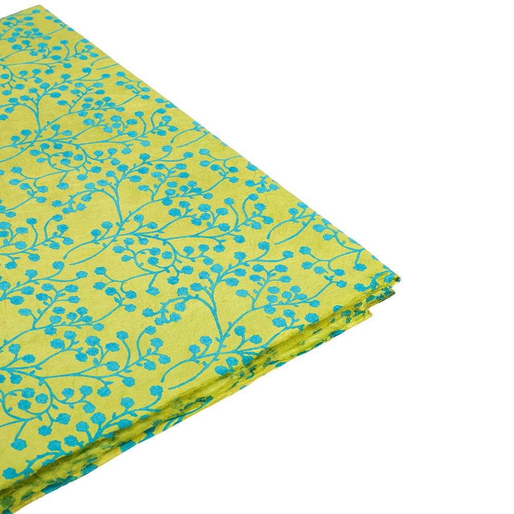 Gefaltetes gelbes Nepalpapier von ☆ mit blauem Blumen- und grünem Blütenranke-Muster auf weißem Hintergrund - ideal als nachhaltiges Geschenkpapier für umweltfreundliche Verpackungen.