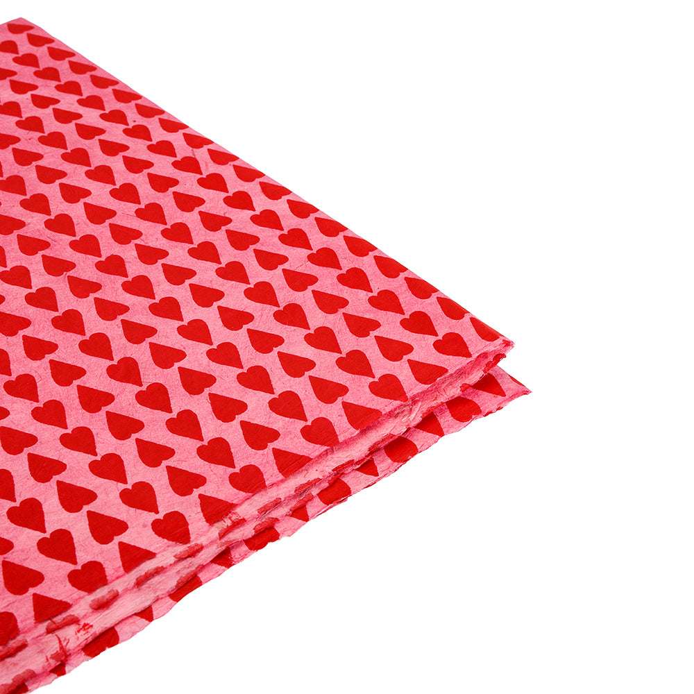 Roter Stoff von ☆ mit einem sich wiederholenden roten Herzmuster auf einem helleren roten Hintergrund und an der Ecke gefaltet - nachhaltiges Geschenkpapier mit handgefertigtem Charme, das an Nepalpapier erinnert.