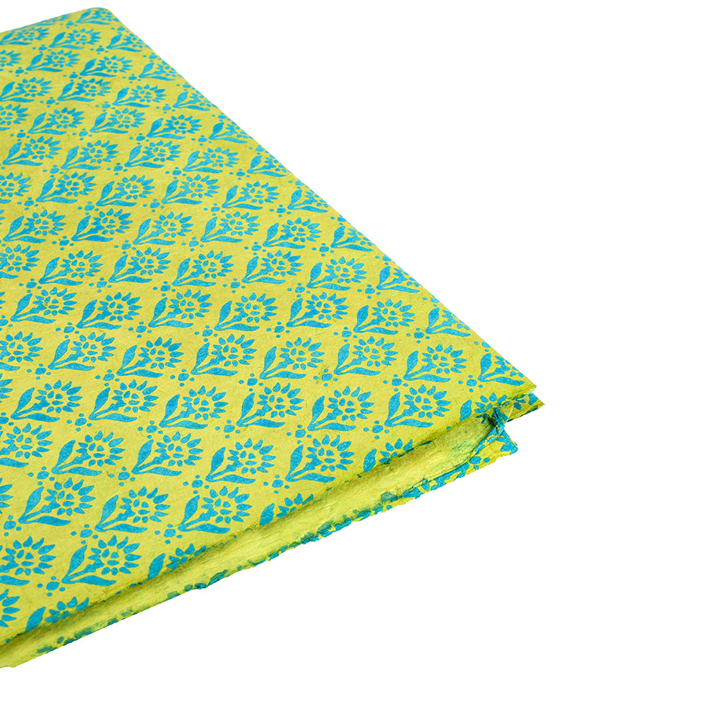 Gefalteter gelber Stoff mit einem blauen Blumenblockdruck auf weißem Grund, der an die lebhaften Muster von ☆ Nepalpapier grün und nachhaltigem Geschenkpapier erinnert.