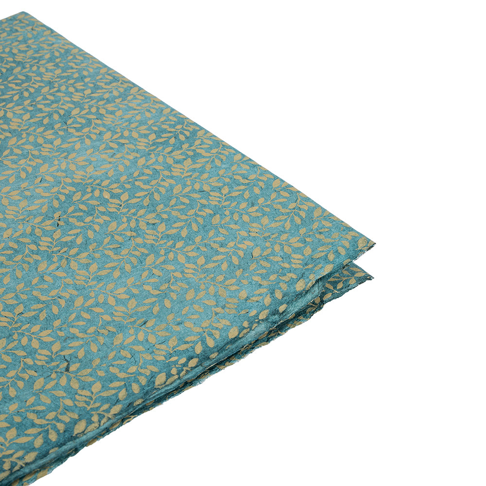 Gefalteter tealfarbener Stoff mit Blattgoldmuster von ☆, auf weißem Hintergrund - erinnert an Nepalpapier und ist ideal als nachhaltiges Papier oder einzigartiges Geschenkpapier für besondere Anlässe.