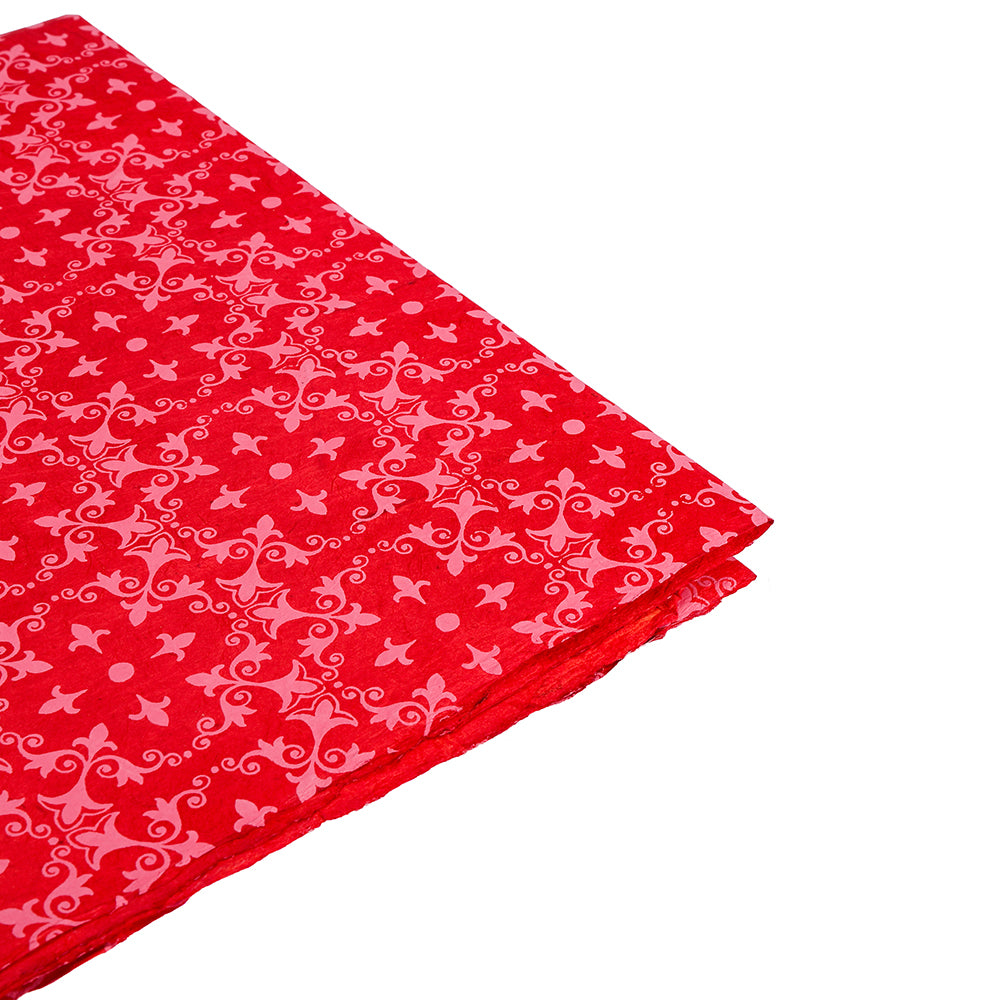 Gefalteter roter Stoff mit einem rosafarbenen, verschnörkelten Blumenmuster, das an die nachhaltige Nepalpapier Geschenkverpackung von ☆ erinnert, auf weißem Hintergrund.