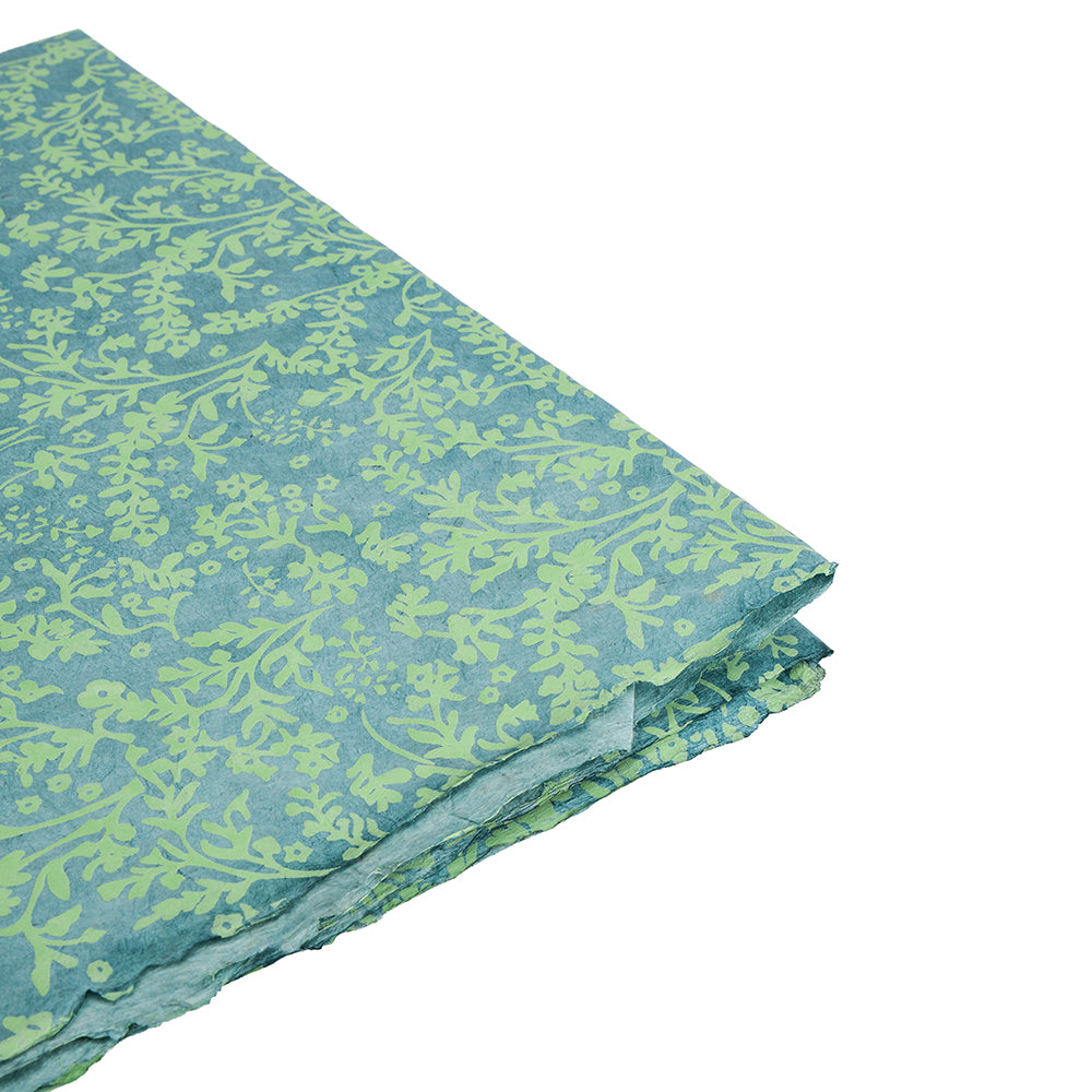 Gefaltetes grün-blau gemustertes Nepalpapier mit botanischem Blattmuster auf weißem Hintergrund von ☆-ideal als nachhaltiges Geschenkpapier für umweltbewusstes Verschenken.