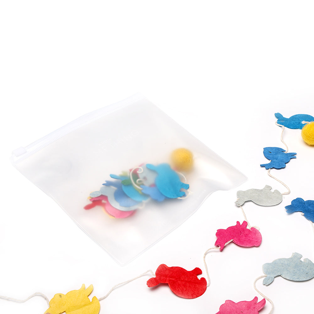 Eine durchsichtige Reißverschlusstasche von ☆ mit farbenfrohen Tierformen aus Filz und einer handgefertigten Papiergirlande, alles vor einem weißen Hintergrund.