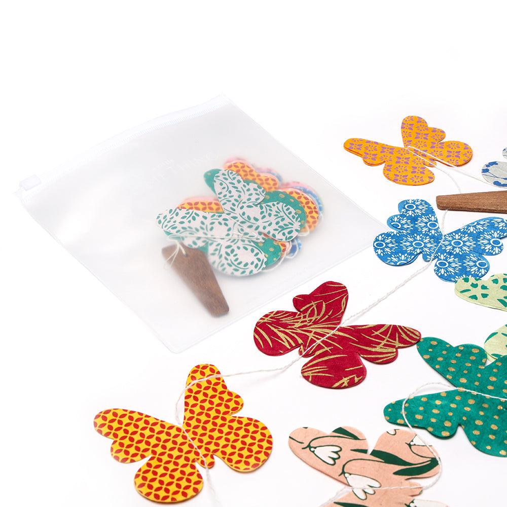 ☆ Bunte Papierschmetterlinge und Holzteile neben einem weißen Reißverschlussbeutel - ideal als handgefertigte Dekoration oder zum Basteln einer nachhaltigen Girlande aus Girlanden Nepalpapier.