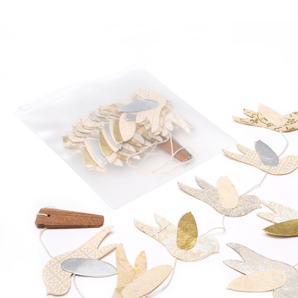 Eine handgemachte Papiergirlande von ☆ aus Nepalpapier mit goldenen und silbernen Akzenten liegt neben einem transparenten Aufbewahrungsbeutel - nachhaltige Dekoration für Ihr Zuhause.