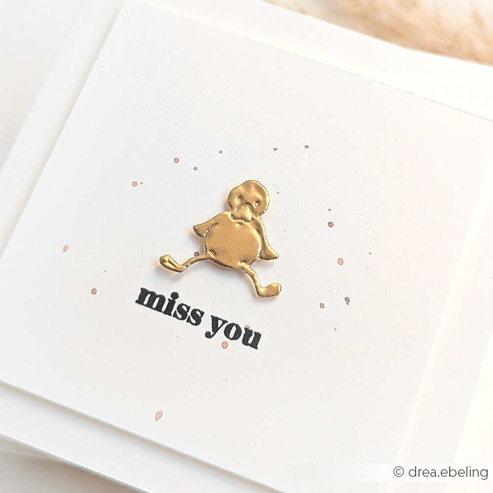 Ein goldgeprägtes Küken, gefertigt mit Prägefolie aus Aluminium von Alexandra Renke, sitzt über "miss you" auf einer weißen Karte mit winzigen rosa Punkten und zarten goldenen Akzenten.