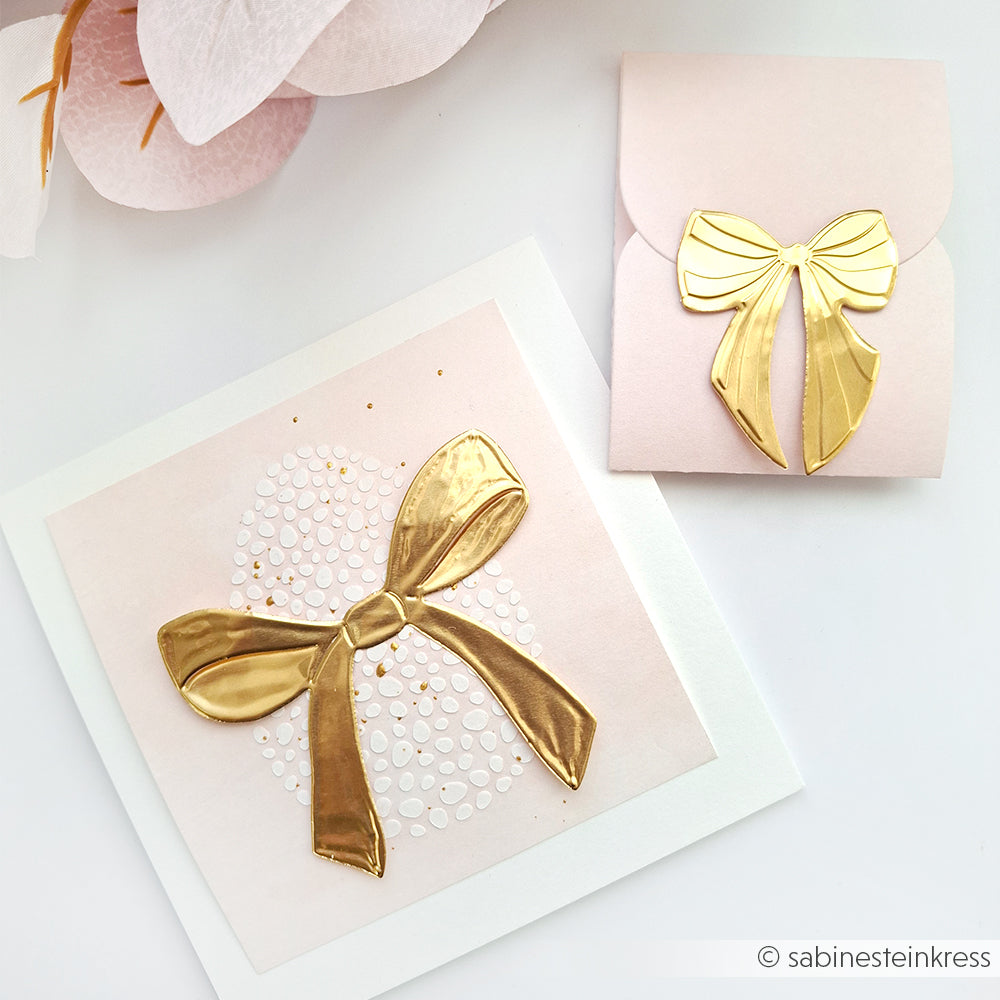 Quadratische Karte und Umschlag von Alexandra Renke, jeweils verziert mit einer glänzenden goldenen Schleife und goldenen Akzenten auf zartem Rosa - ideal zum Basteln oder um mit geprägter Alufolie einen kreativen Akzent zu setzen.