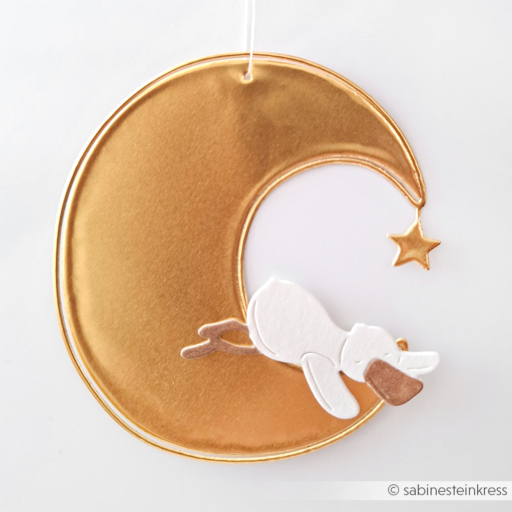 Goldene Mondsichel von Alexandra Renke mit einem kleinen weißen Hasen und einem hängenden Stern, der an einer weißen Schnur aufgehängt ist - ideal für Bastelarbeiten oder um goldene Akzente in Ihrer Einrichtung zu setzen.