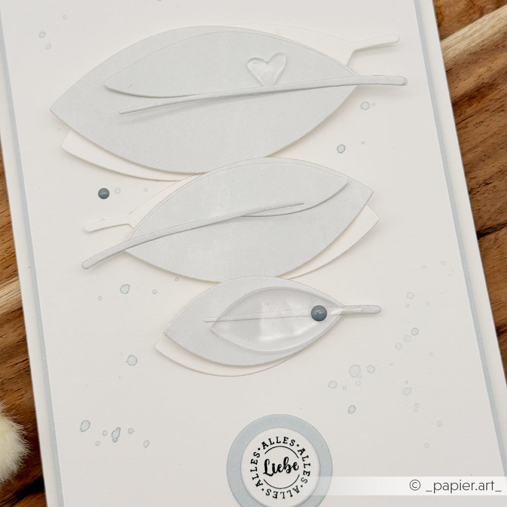 Dreischichtige Papierblätter mit minimalistischem Design, einem kleinen Herz und einem gestempelten Text auf einer weißen Karte mit grauen Punkten – die perfekte Inspiration, wenn Sie Schmuck selbst gestalten oder Anhänger selbst basteln möchten und dabei Ihrer eigenen Kreativität freien Lauf lassen wollen.