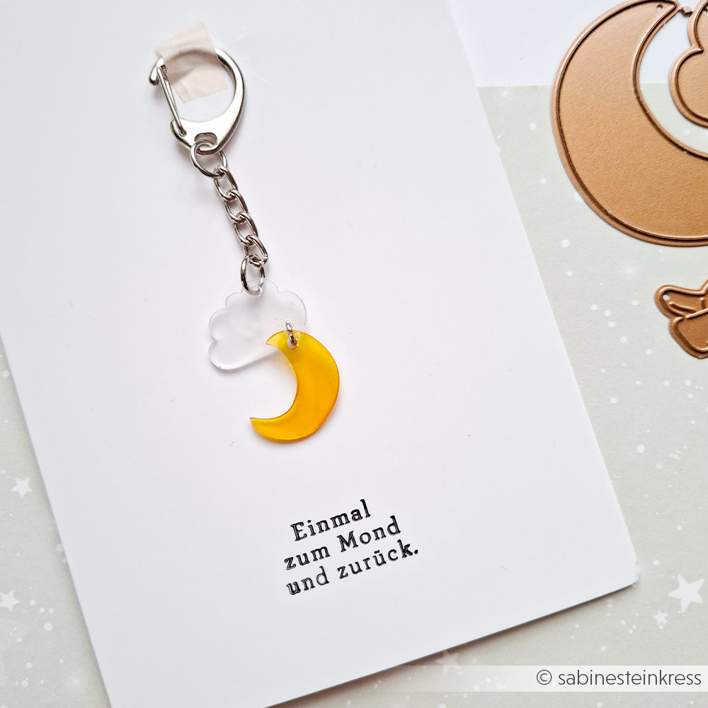 Schlüsselanhänger mit einem gelben Halbmond und einer weißen Wolke, liebevoll aus Schrumpffolie gefertigt, an einer Karte mit der Aufschrift „Einmal zum Mond und zurück“. Perfekt für alle, die gerne Schmuck selbst basteln und einzigartige Accessoires lieben.