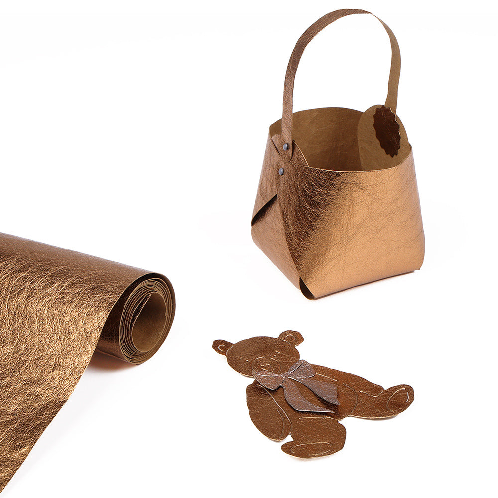 Eine Rolle Alexandra Renke PAPP-Papier in Metallicbraun, ein passender Papierkorb und ein Bärenausschnitt für die Kartengestaltung sind auf einer weißen Fläche ausgestellt.