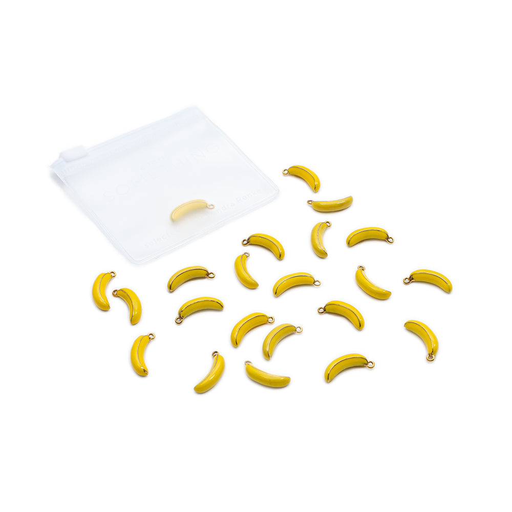 Zwanzig kleine gelbe Bananen-Anhänger von Alexandra Renke sind neben einem durchsichtigen Beutel mit Reißverschluss auf weißem Hintergrund verstreut.