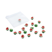 Kleine, wassermelonenförmige „Obst“-Charms und Anhänger von Alexandra Renke, verstreut auf einer weißen Fläche, im Hintergrund ist ein durchsichtiges Reißverschluss-Säckchen zu sehen.
