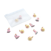 Zehn kleine rosa und gelbe Anhänger in Form von Hüten und Stiefeln aus dem Alexandra Renke Charm-Set sind neben einem durchsichtigen Beutel mit weißem Reißverschluss vor einem weißen Hintergrund abgebildet.