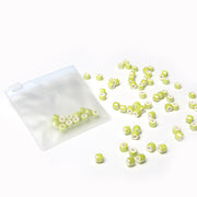 Kleine grün-weiß glasierte Keramikperlen von Alexandra Renke sind in einem transparenten, wiederverschließbaren Beutel auf weißem Hintergrund verstreut - ideal für Perlen basteln oder Schmuck selber machen.