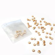 Kleine hellbraune und weiß glasierte Keramikperlen von Alexandra Renke sind neben einem durchsichtigen Reißverschlussbeutel auf weißem Hintergrund verstreut, ideal für die Schmuckherstellung und Perlenbastelprojekte.