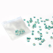 Ein kleines durchsichtiges Täschchen von Alexandra Renke mit türkis und weiß glasierten Keramikperlen, einige davon außen verstreut - ideales Schmuckzubehör für alle, die gerne Schmuck herstellen.