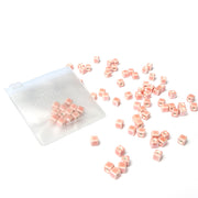 Kleine rosafarbene Perlen zum Auffädeln von Alexandra Renke sind neben einem durchsichtigen Reißverschlussbeutel auf weißem Grund verstreut - ideal, um Schmuck selbst zu machen.