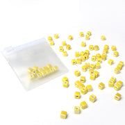 Kleine gelbe Keramikperlen-Würfel von Alexandra Renke verstreut neben einem durchsichtigen Reißverschlussbeutel auf weißem Hintergrund - ideal für glasierte Schmuckgestaltungsprojekte.