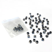 Kleine schwarze, glasierte würfelförmige Keramikperlen mit weißen Punkten von Alexandra Renke, teils verstreut und teils in einem durchsichtigen Zip-Beutel auf einer weißen Fläche - ideal für Schmuck selber machen.