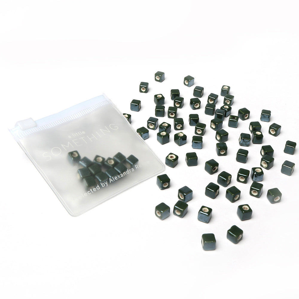 Kleine schwarz glasierte Keramikperlen von Alexandra Renke liegen verstreut neben einem durchsichtigen, wiederverschließbaren Beutel - ideal zum Perlen Auffädeln und Schmuck gestalten.