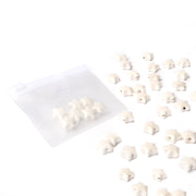 Kleine weiße Sternform-Perlen von Alexandra Renke, die wie glasierte Keramik aussehen, sind neben einem durchsichtigen Ziplock-Beutel auf weißem Hintergrund angeordnet - perfekt, wenn Sie Schmuck selbst machen möchten.
