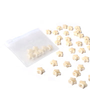 Alexandra Renke kleine, beigefarbene Bonbons in Sternform, die aus einem durchsichtigen, wiederverschließbaren Beutel auf eine weiße Oberfläche tropfen - ideal, um sie selbst zu machen und Ihren Kreationen einen skurrilen Touch zu verleihen.